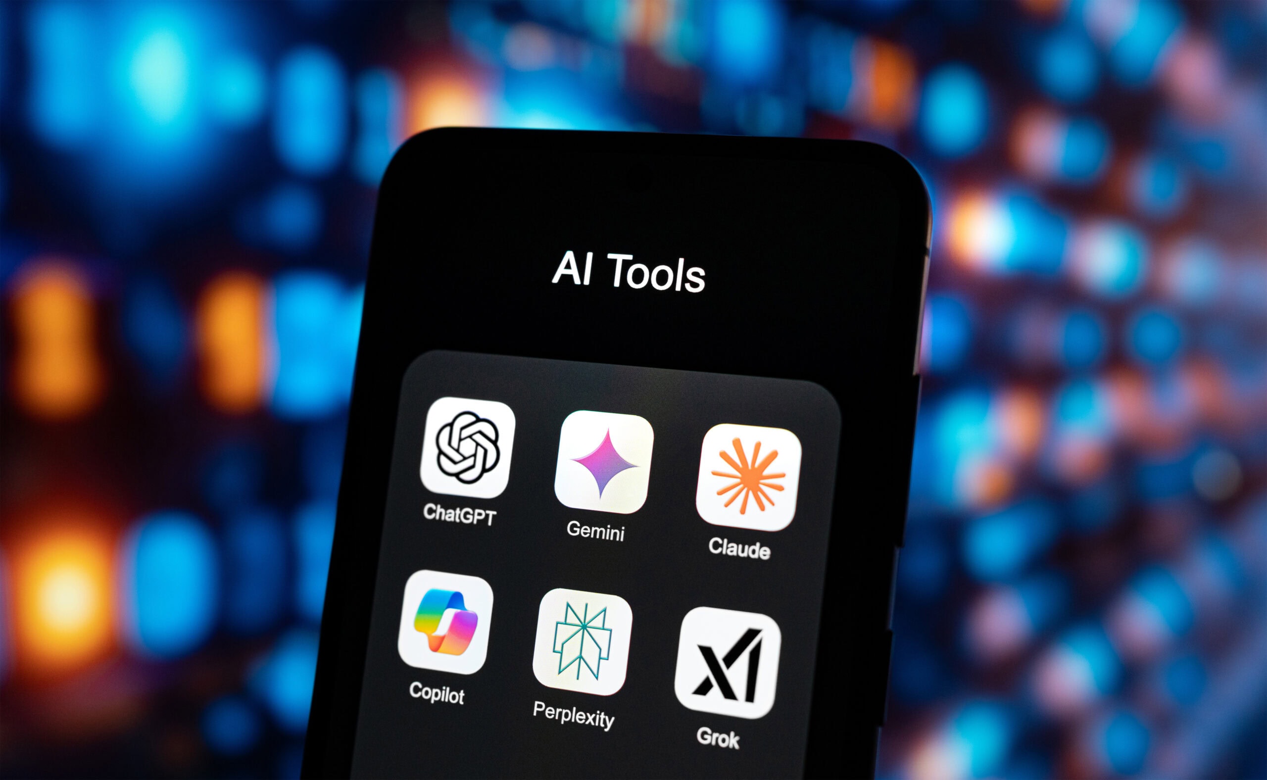 Smartphone-Bildschirm mit geöffnetem Ordner „AI Tools“, der Icons von ChatGPT, Gemini, Claude, Copilot, Perplexity und Grok zeigt, vor unscharfem, buntem Lichterhintergrund.