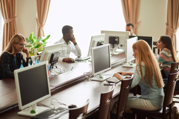 Mehrere Personen arbeiten in einem offenen Raum an Desktop-Computern – Symbolbild für potenzielle Sicherheitsrisiken in öffentlichen WLAN- oder Arbeitsumgebungen.