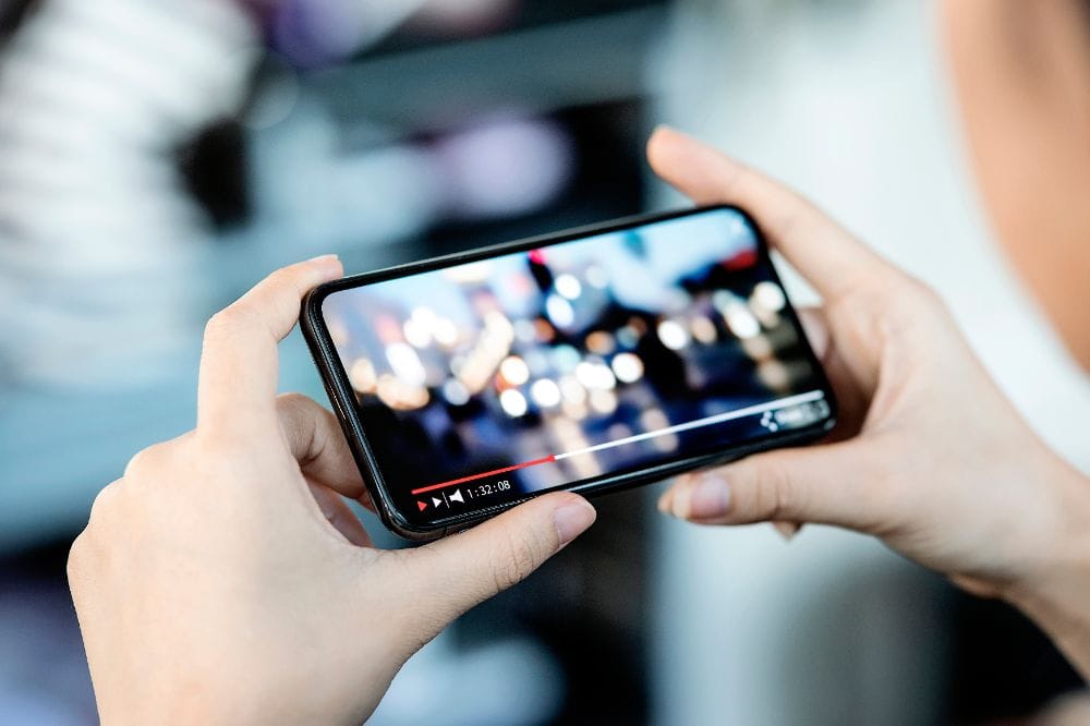 Person hält Smartphone quer in den Händen und schaut ein Video, das bereits seit 1 Stunde 32 Minuten läuft.