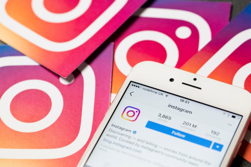 Smartphone mit geöffneter Instagram-App, umgeben von mehreren Instagram-Logos auf farbigem Hintergrund