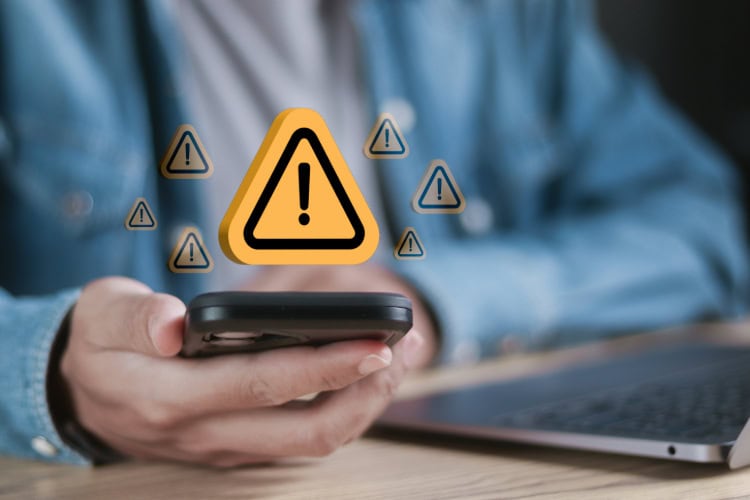 Person hält ein Smartphone in der Hand, über dem mehrere Warnsymbole mit Ausrufezeichen schweben – Symbolbild für eine Sicherheitswarnung oder Datenleck.