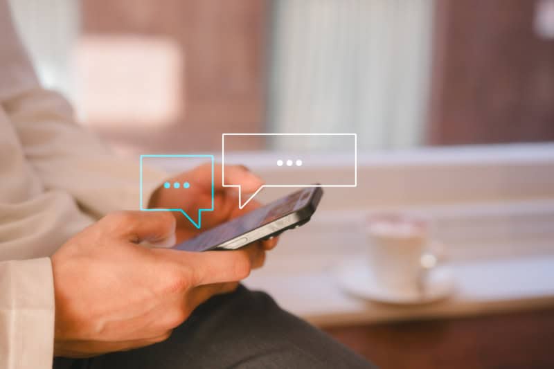 Person tippt auf einem Smartphone, darüber sind zwei stilisierte Sprechblasen eingeblendet.