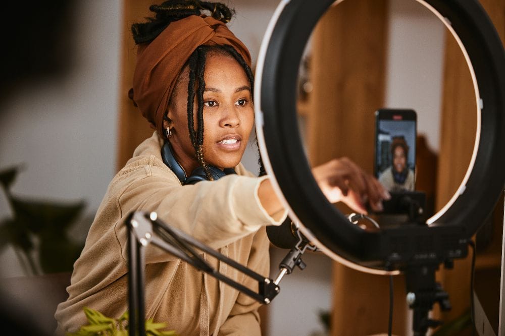 Frau nimmt mit Smartphone und Ringlicht ein Video auf, professionelle Content-Produktion in einem Heimstudio.