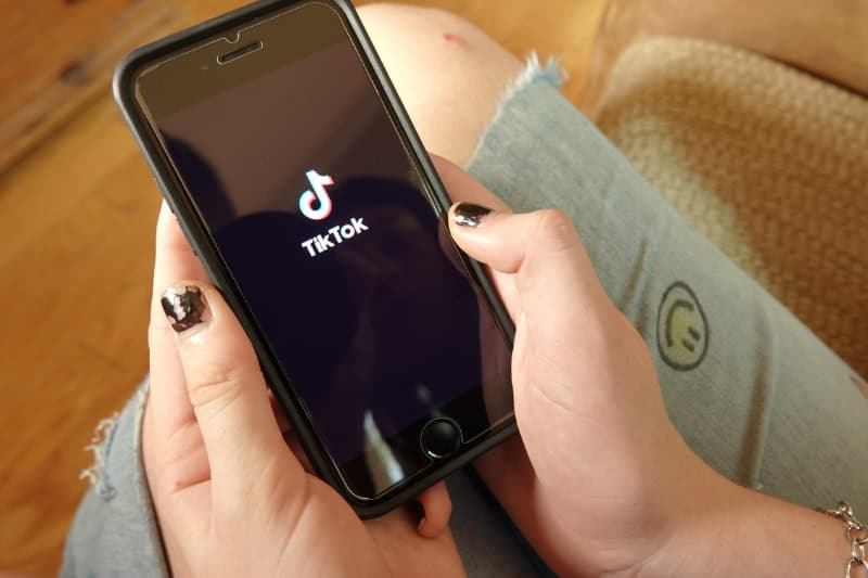 Eine junge Frau mit lackierten Fingernägeln öffnet auf ihrem Handy die TikTok App.