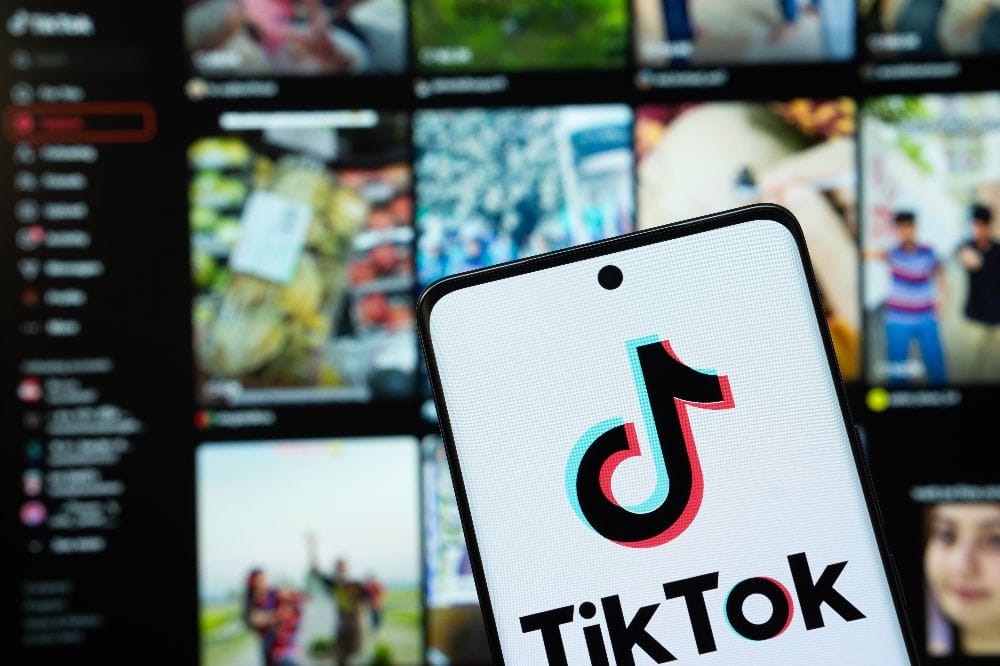 Smartphone mit geöffneter TikTok-App im Vordergrund, unscharfer TikTok-Feed im Hintergrund.